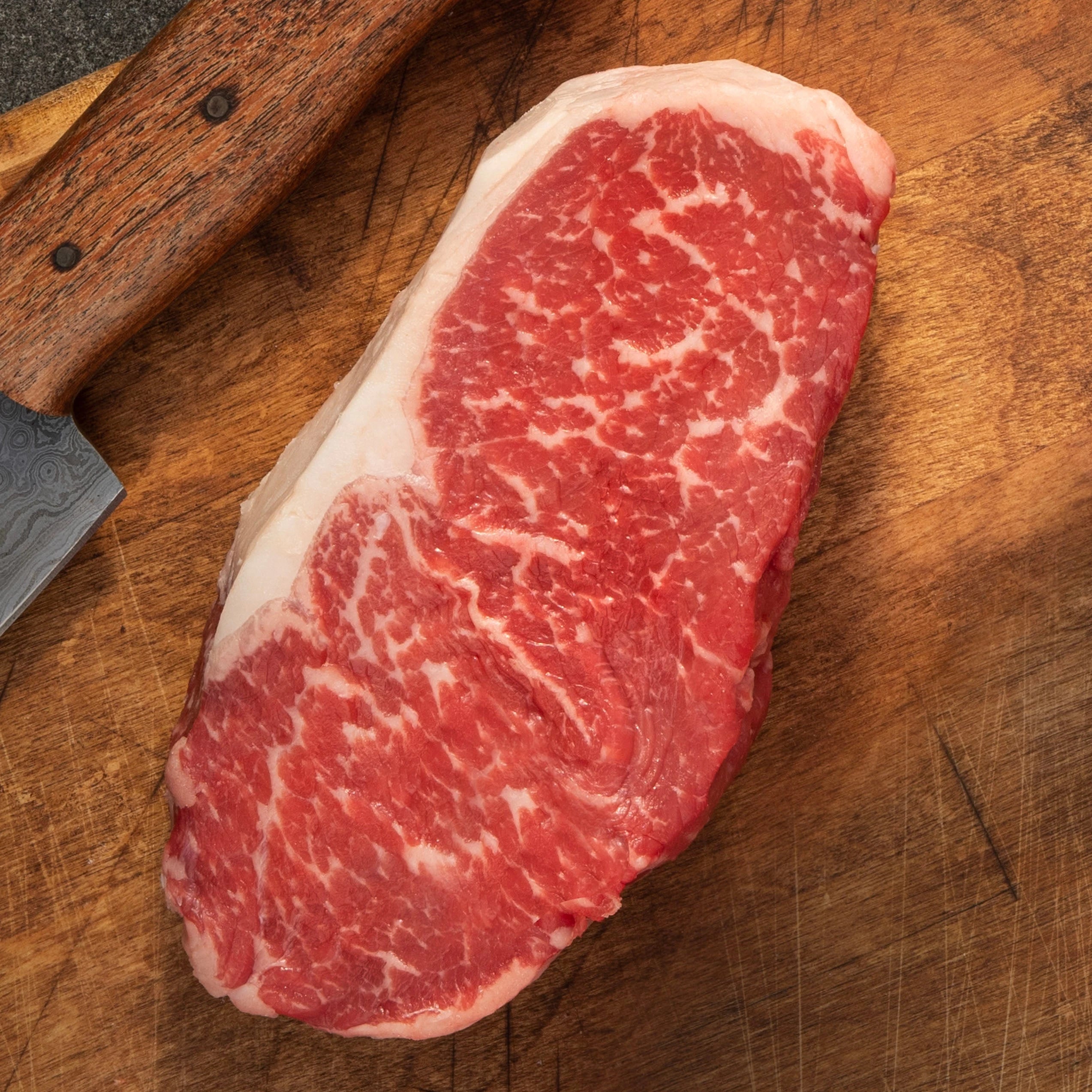 uncooked striploin steak cut on cutting board with steak knife