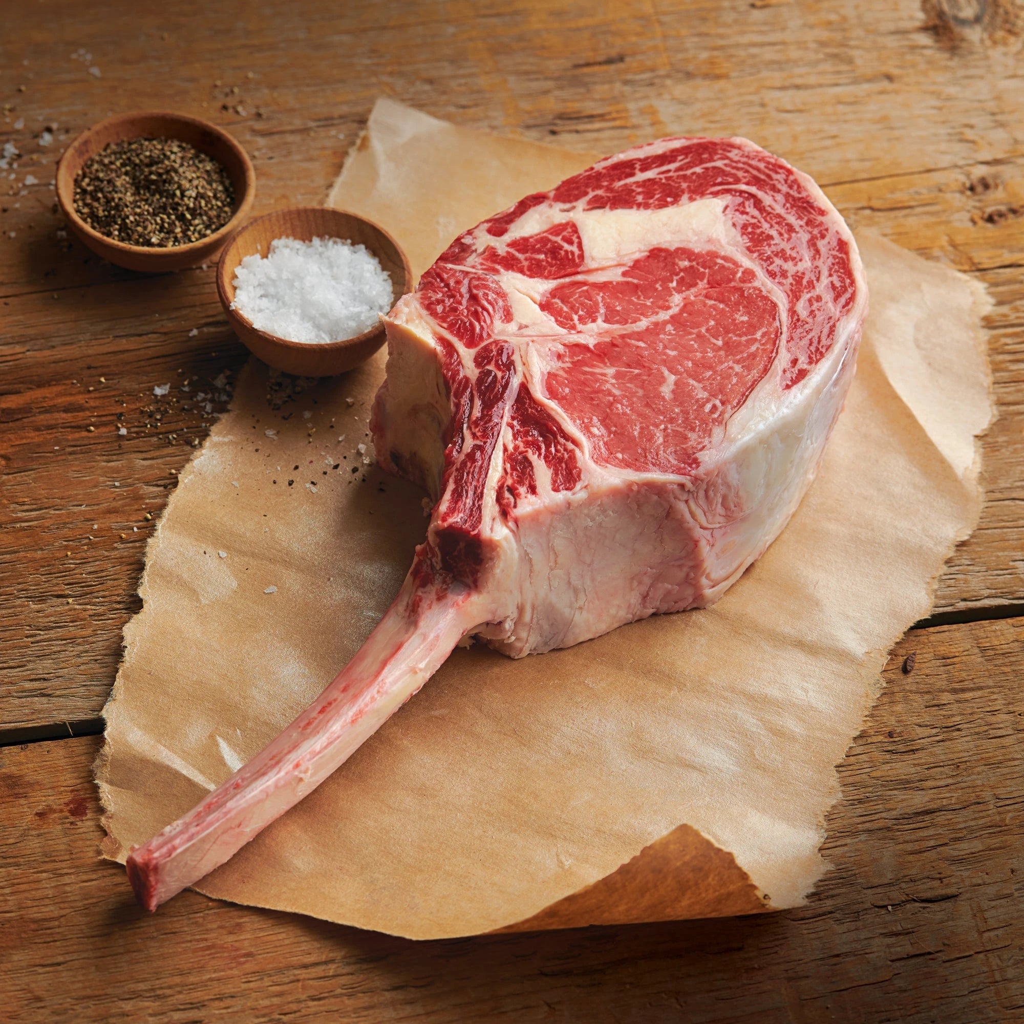 bone-in steak on parchment paper with sea salt and pepper 